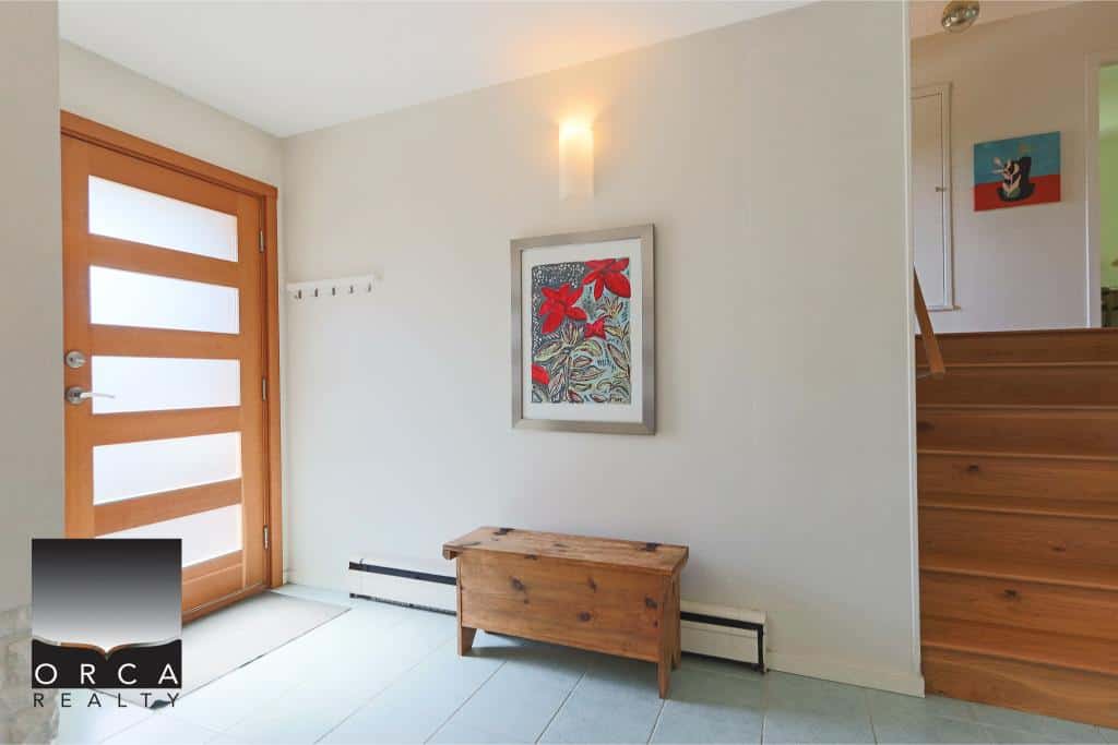 Modern entrance area with wooden door, art decor, and minimalist design, featuring natural wood accents and bright lighting.