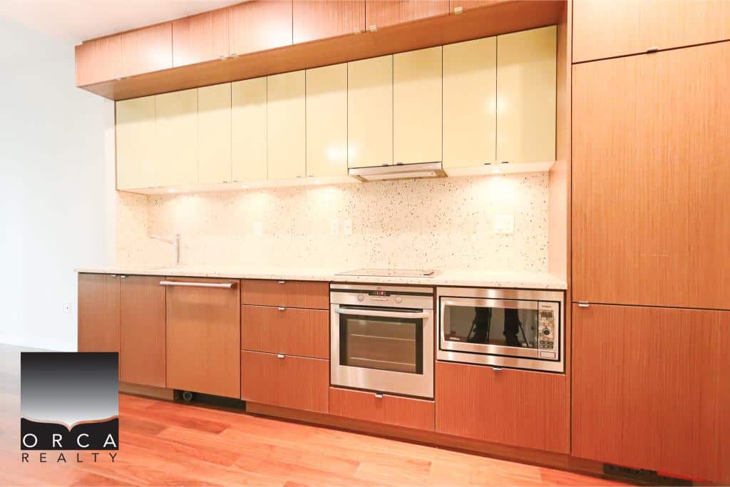 A modern kitchen with wooden cabinets, built-in stainless steel oven, microwave, and a clean backsplash, perfect for contemporary Vancouver homes.