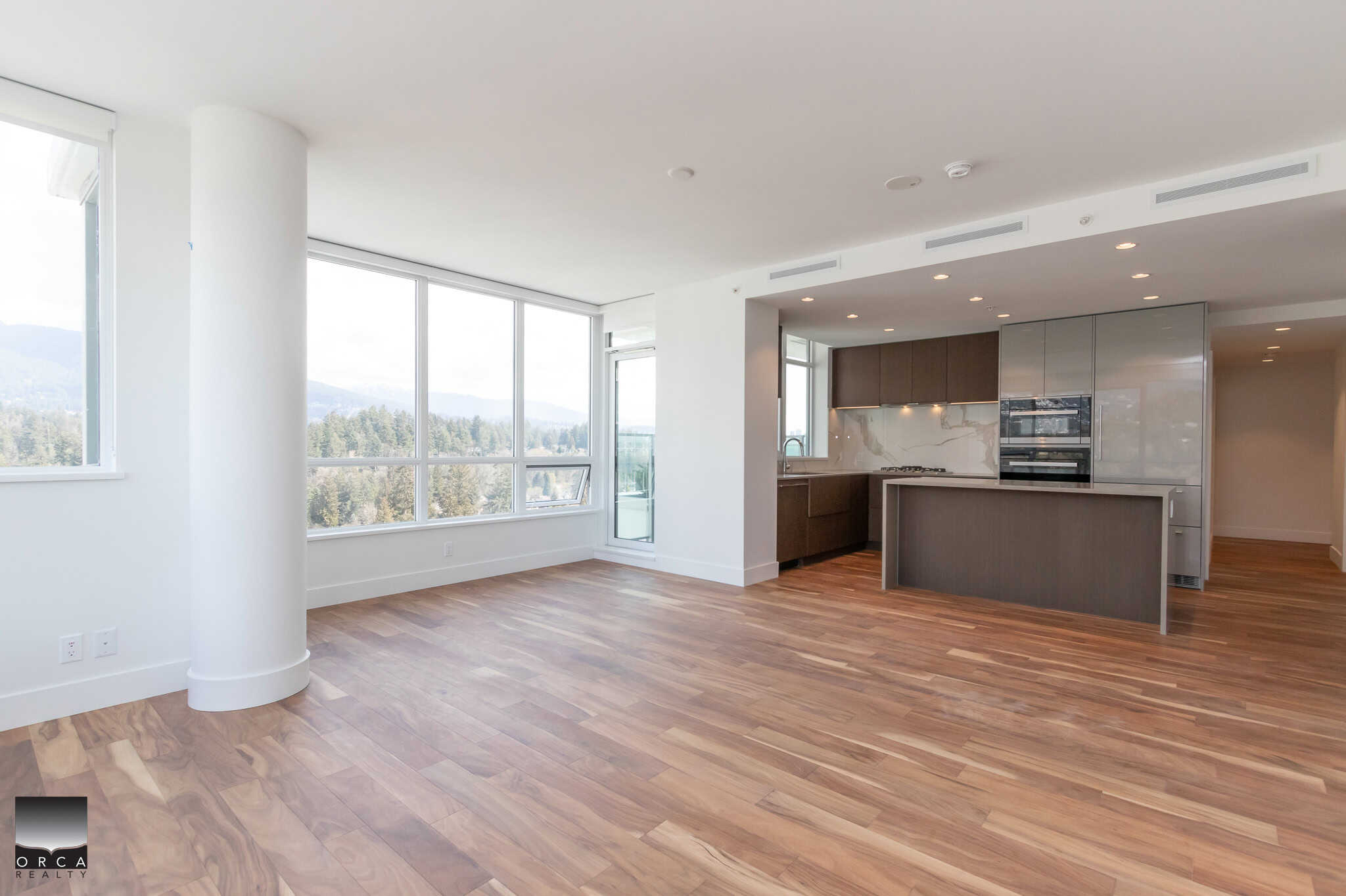 Bright open-concept apartment with large windows showcasing scenic mountain views, modern kitchen with sleek cabinetry, ideal for Vancouver real estate buyers.
