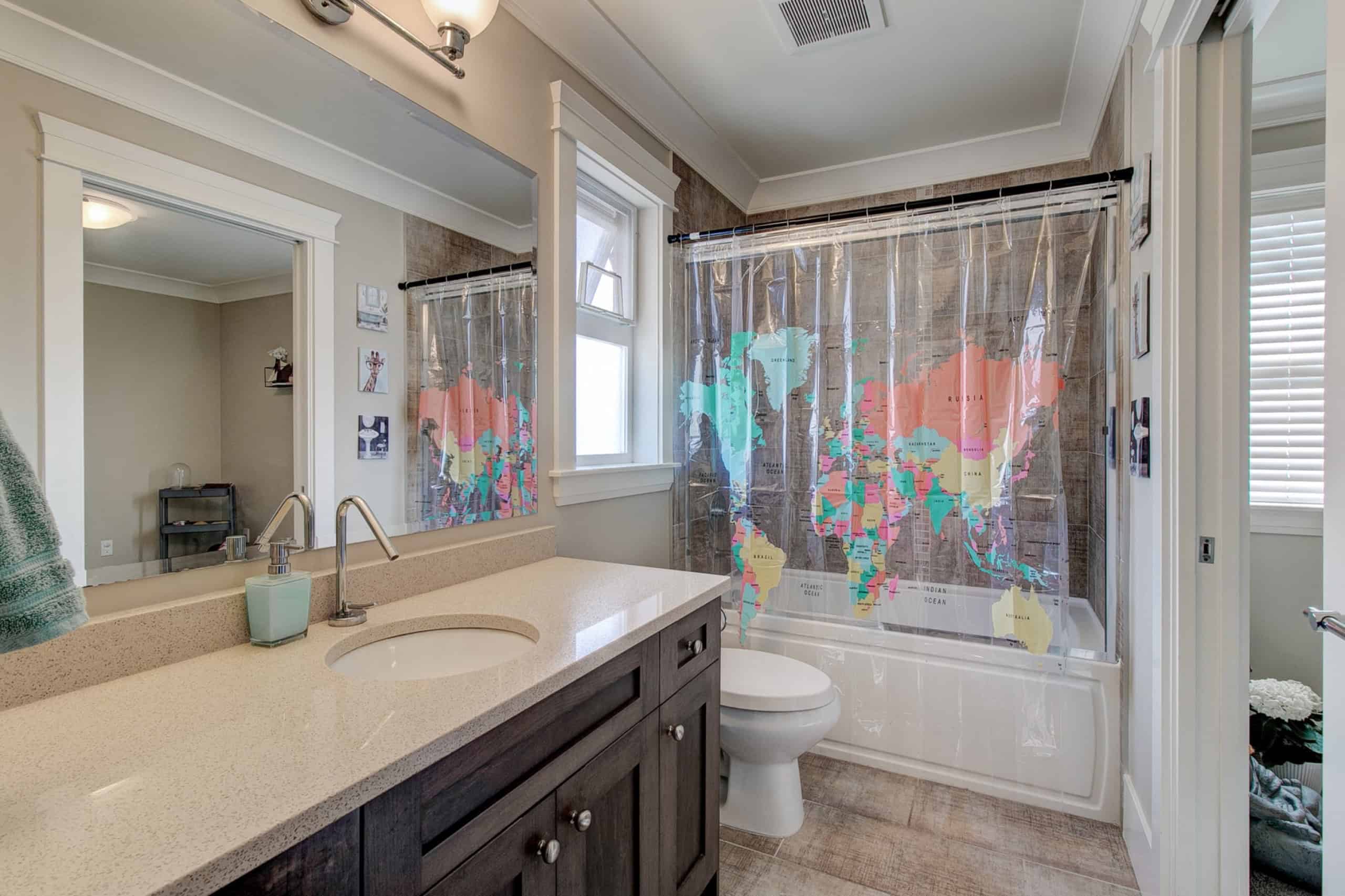 Bright bathroom with a world map shower curtain, beige vanity with a white countertop, and natural light from a window, showcasing Vancouver Island real estate options.
