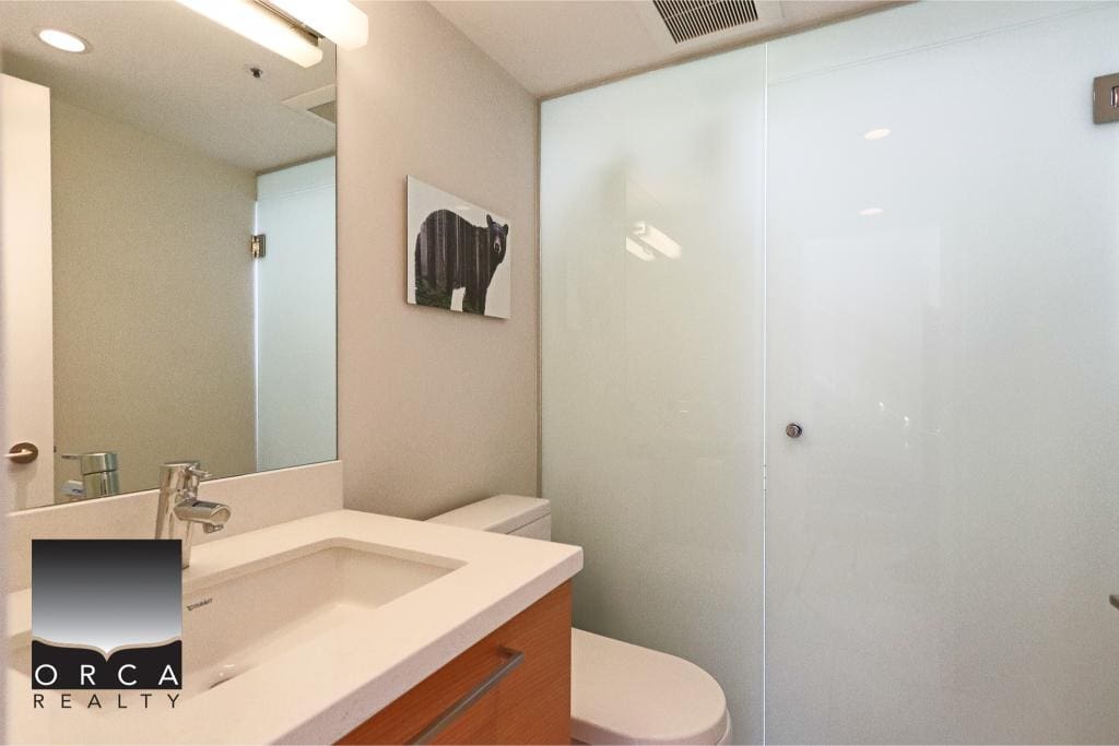 Modern bathroom with glass shower enclosure, white sink, wooden vanity, and minimalist decor, showcasing contemporary Vancouver real estate.