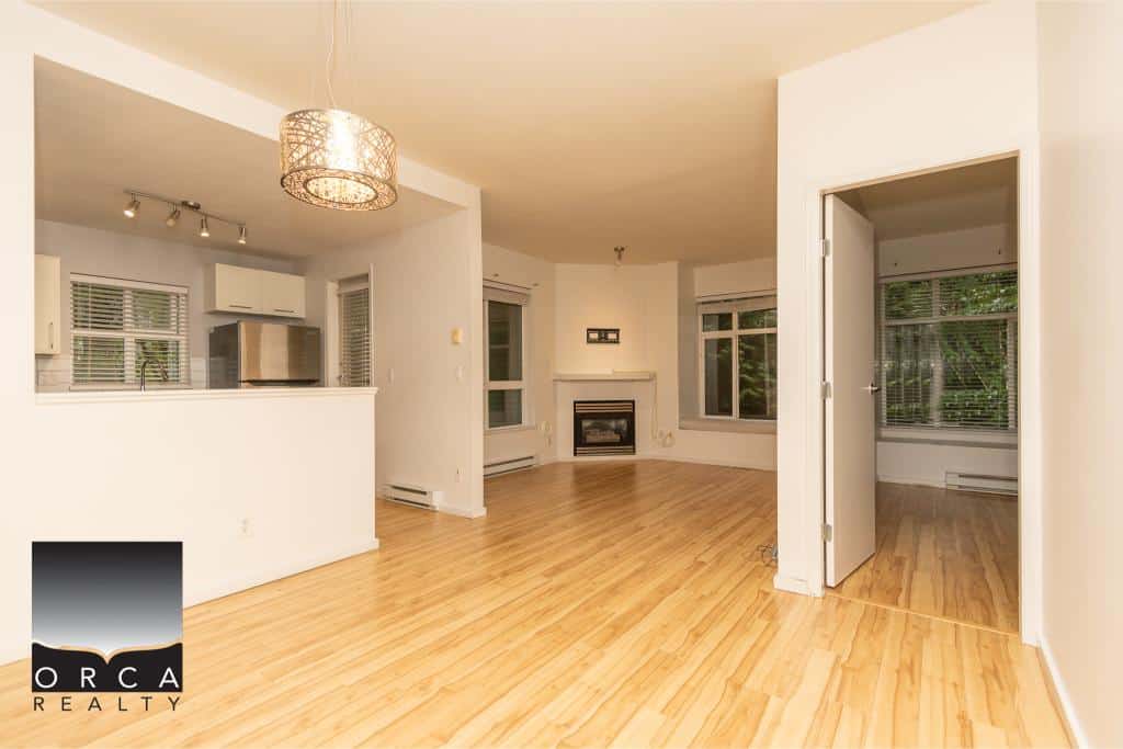 Spacious living room with hardwood floors, large windows, and a cozy fireplace, highlighting an open-concept design in a modern home listing by Orca Realty Inc.
