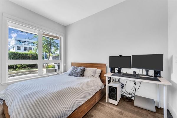 Bright Vancouver bedroom with large window, cozy bed, and dual monitors for work or relaxation.