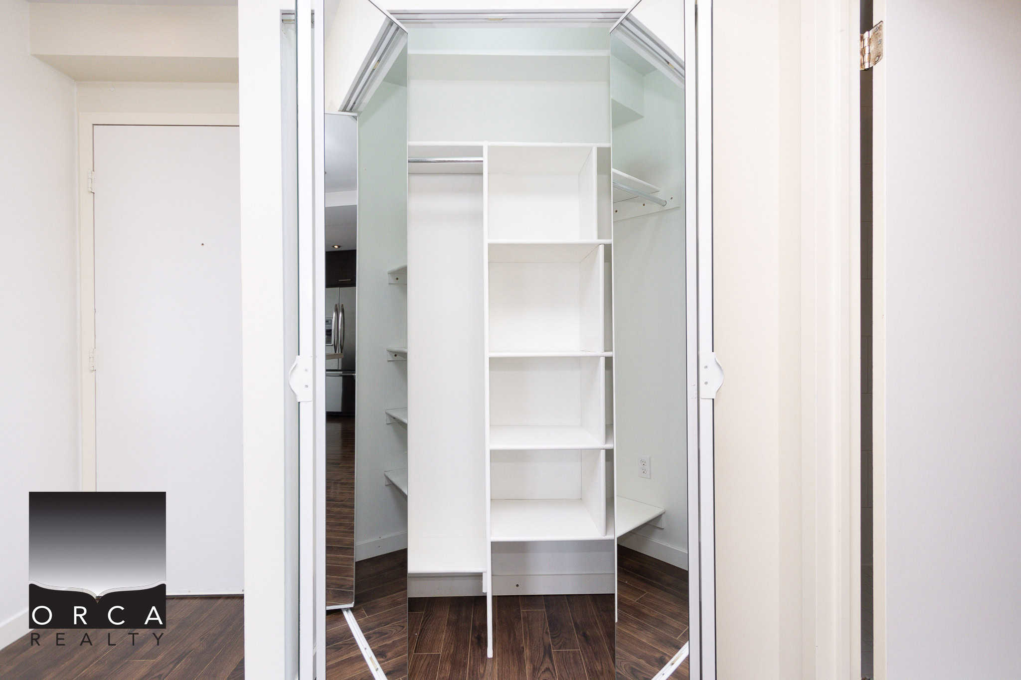 Open walk-in closet with mirrored doors, white shelving, and ample storage space in a modern residential home.