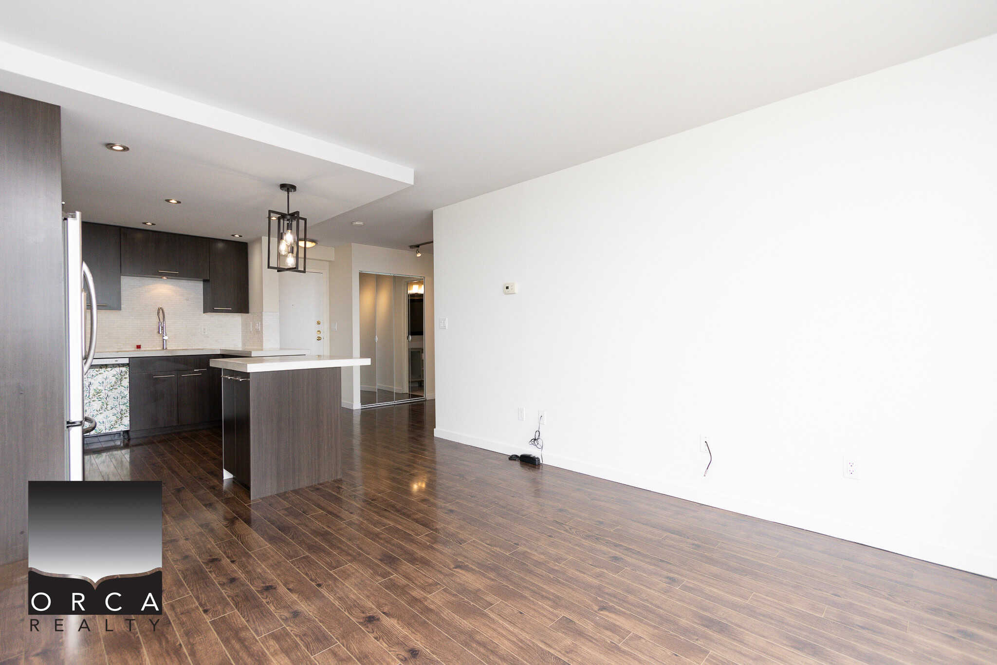 Spacious modern open-concept clear kitchen living area with dark wood flooring, stylish lighting, and minimalist design in a contemporary condo or apartment.