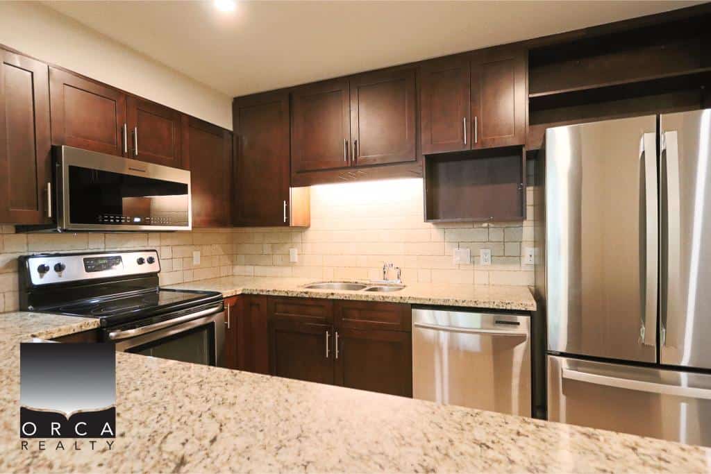 Modern kitchen with dark wood cabinets, stainless steel appliances, granite countertops, and a cozy backsplash, perfect for Vancouver Island homebuyers.