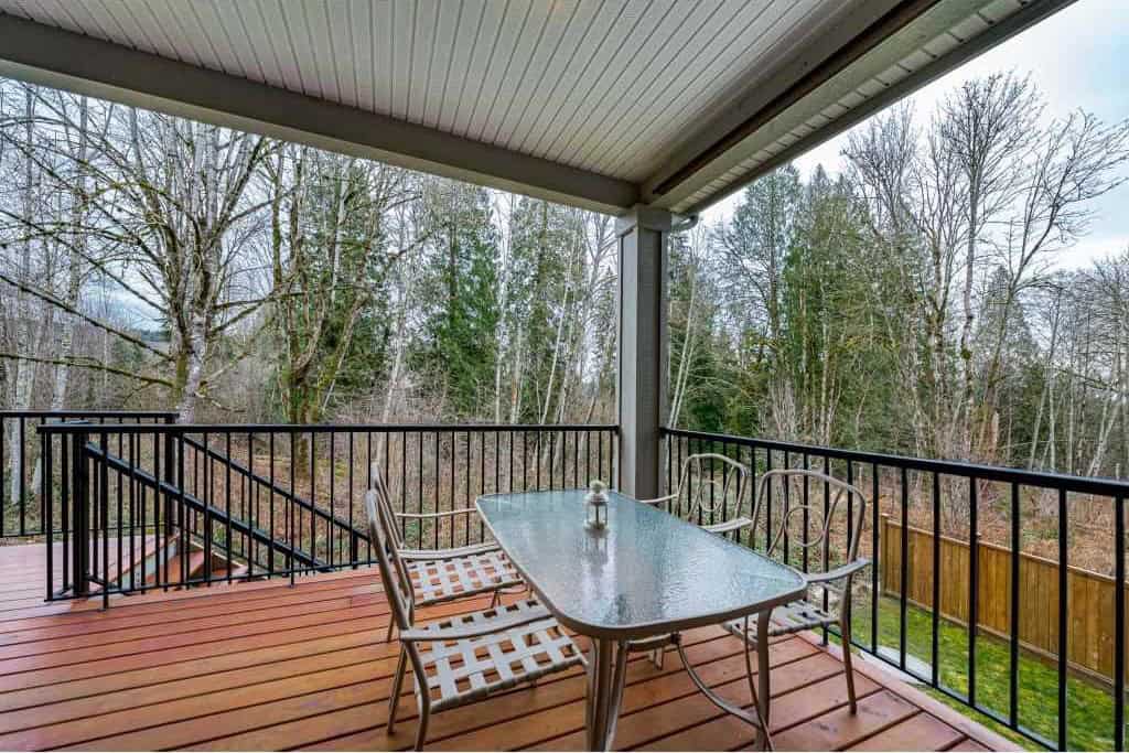 Spacious outdoor balcony with wooden flooring, metal railing, and surrounding trees, ideal for outdoor dining and relaxation.