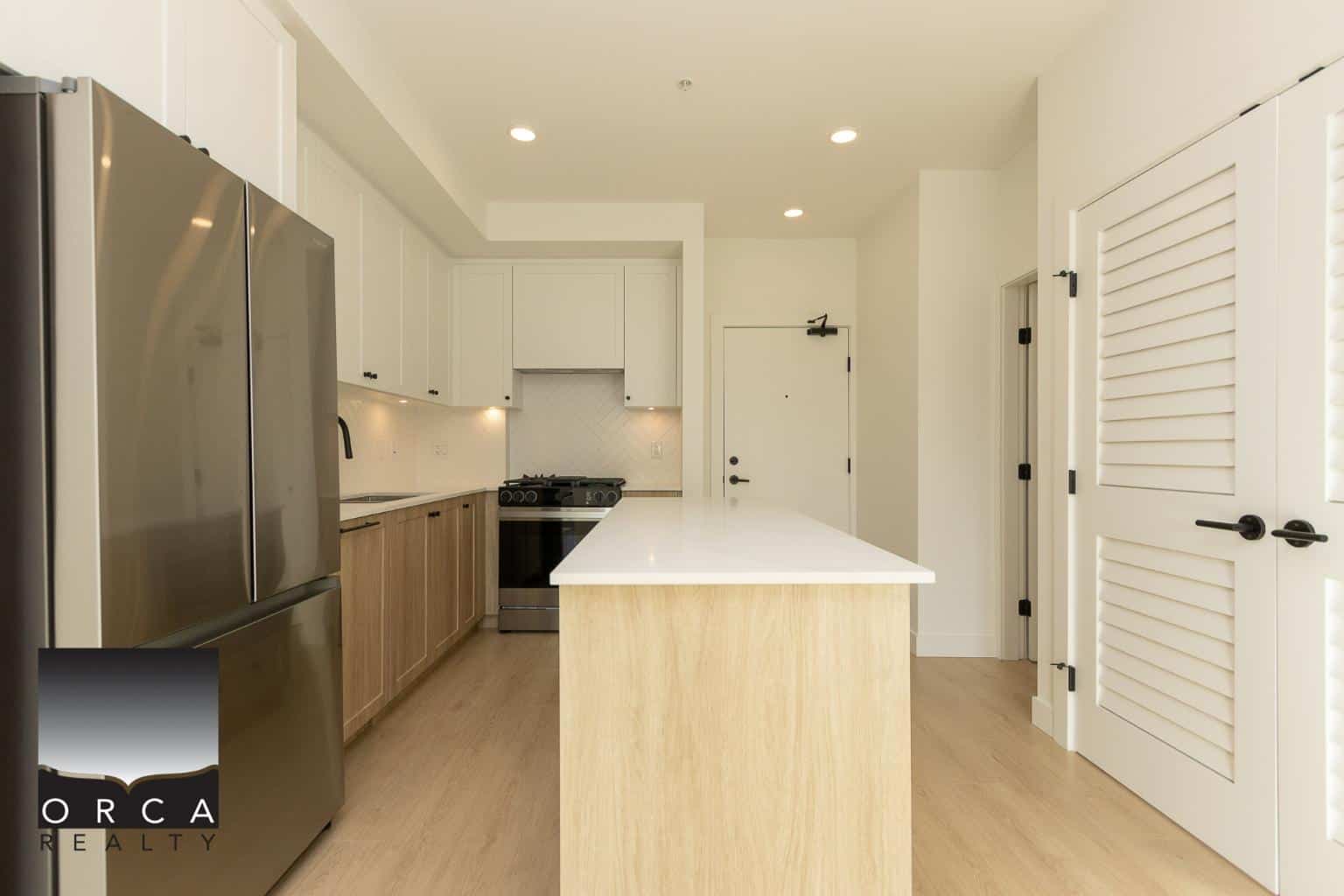 Contemporary modern kitchen with white cabinets, stainless steel appliances, and a spacious white quartz island, perfect for Vancouver Island homebuyers seeking stylish, functional interiors.