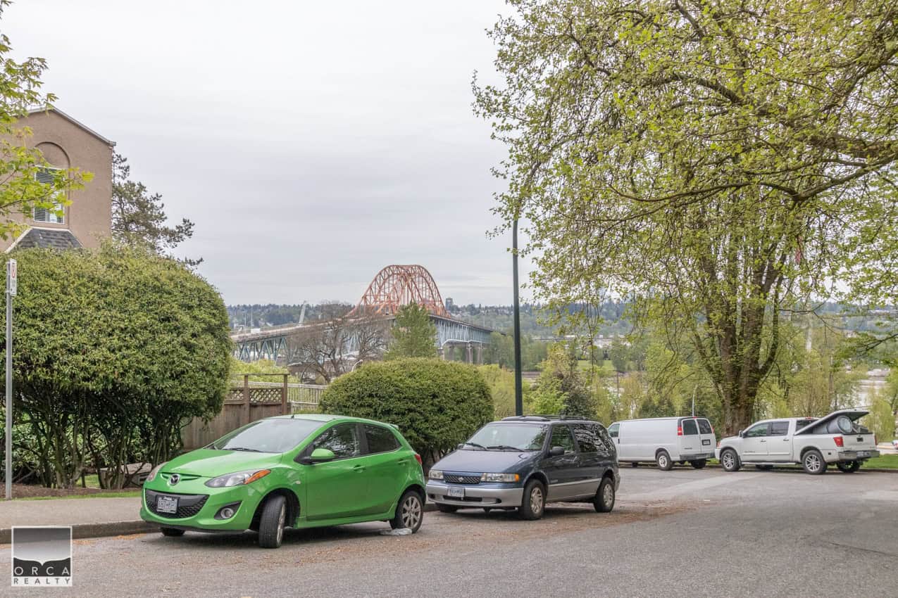 Aerial view of a parking lot with cars, trees, and a cityscape featuring a bridge, showcasing the vibrant community and scenic surroundings relevant to Orca Realty Inc. in Vancouver.