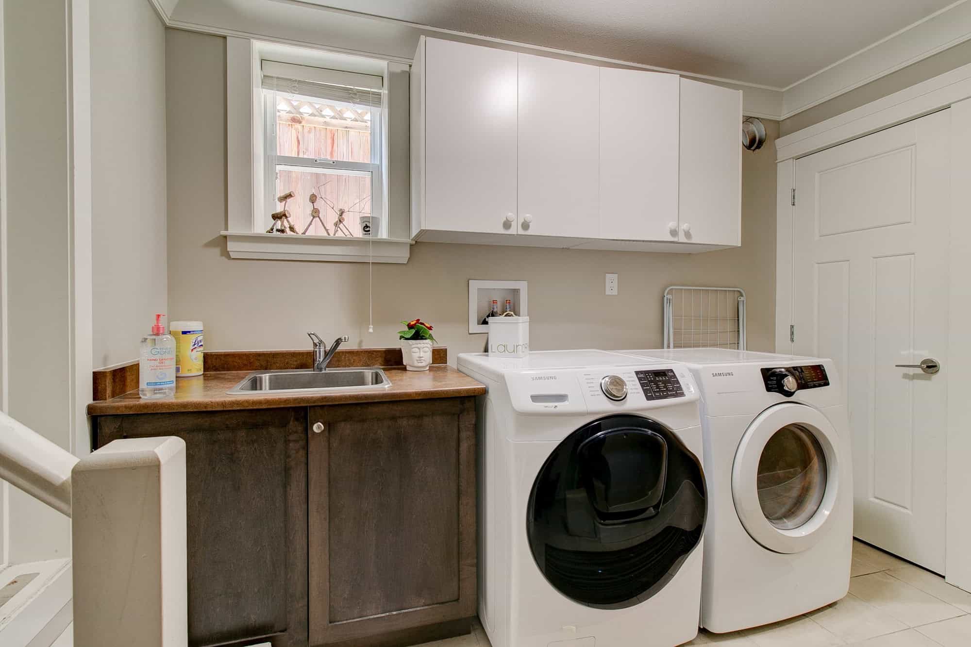 Bright laundry room with washer and dryer, white cabinets, and a cozy utility sink in a modern home. Ideal for convenient household chores, with ample storage and natural light.