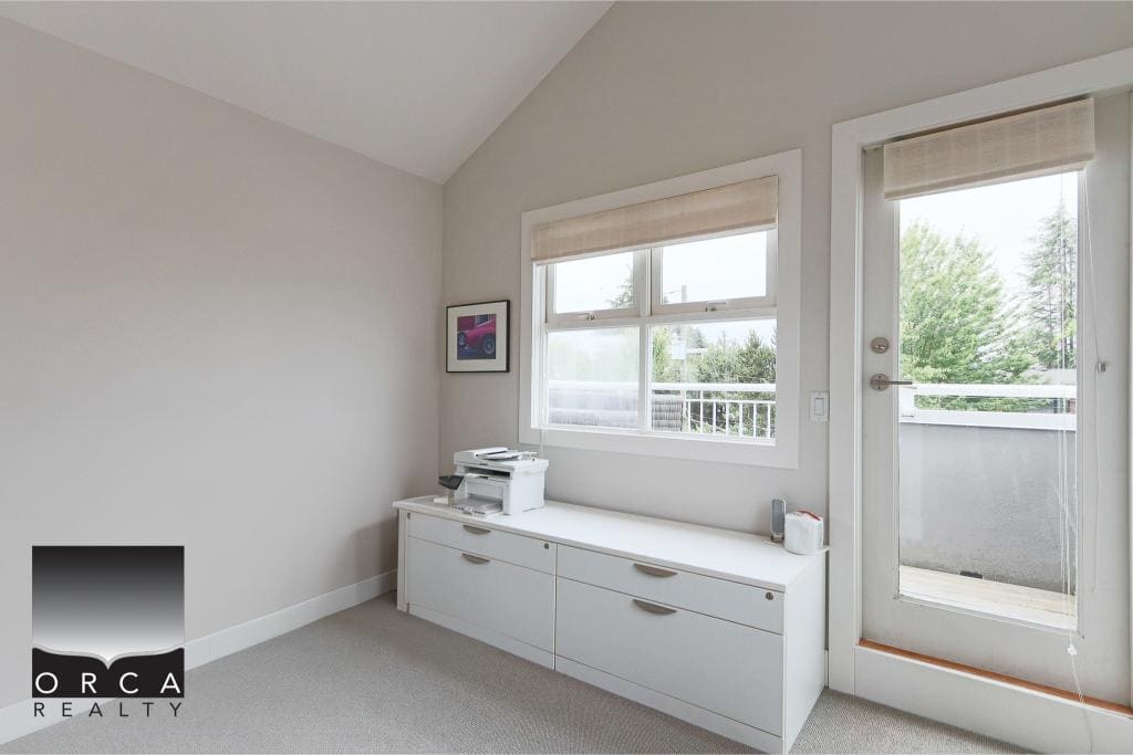 Modern home office with large windows and balcony access, featuring clean white furniture and neutral decor, ideal for remote work or study in Vancouver area.