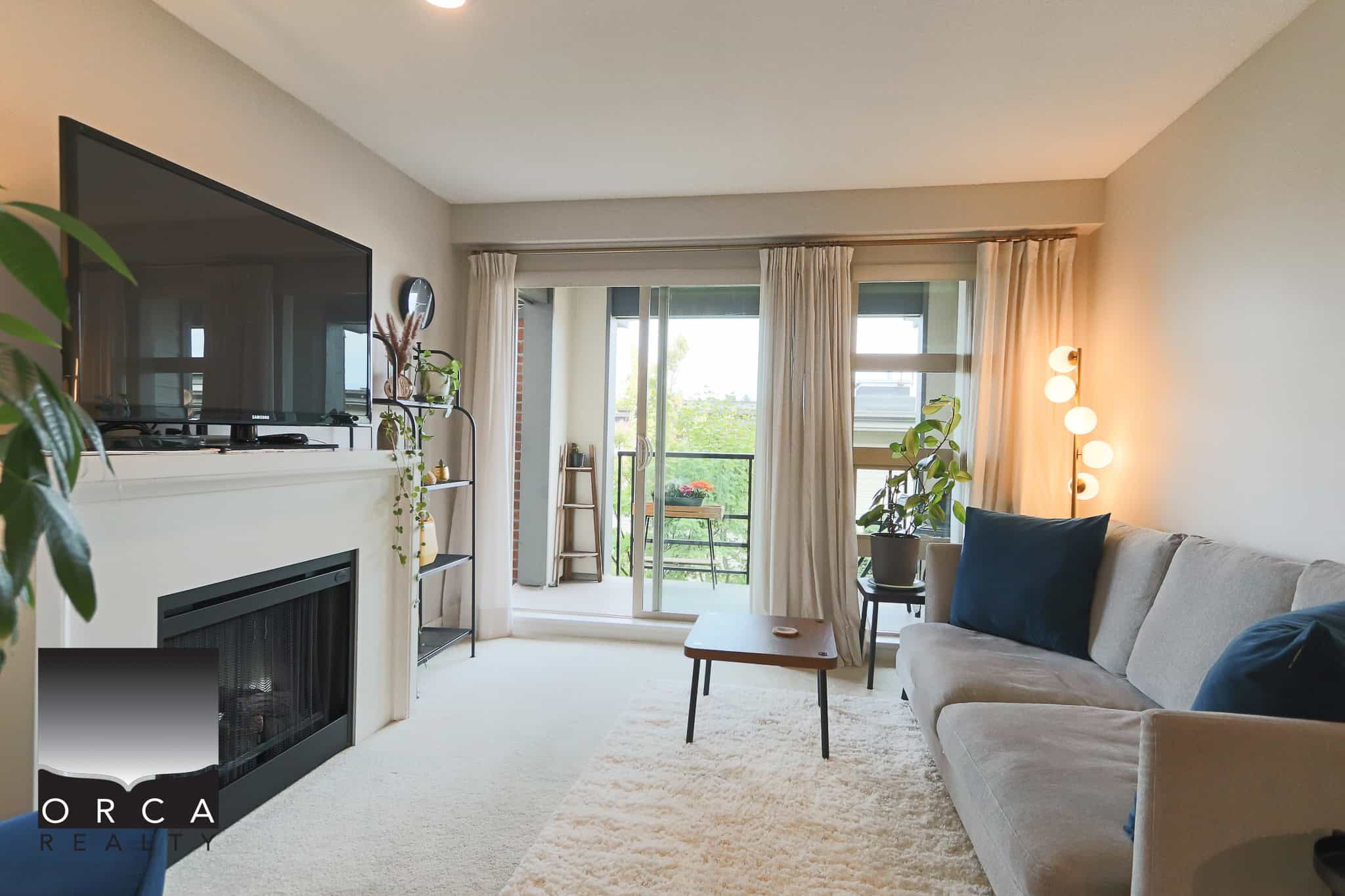 Bright living room with large sliding glass doors leading to a balcony, featuring a cozy beige sofa with navy pillows, modern floor lamp, and indoor plants, showcasing Vancouver area real estate.