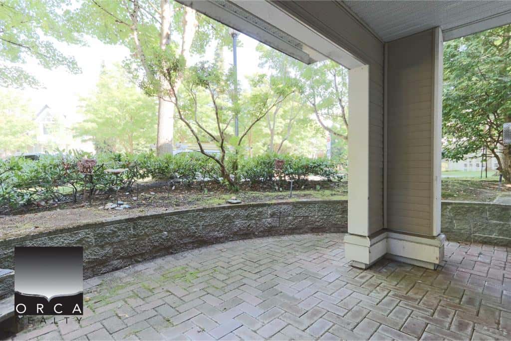 Bright outdoor patio area with brick flooring and lush green landscaping, perfect for relaxing or entertaining in Victoria, BC. Features a covered space and vibrant garden views.