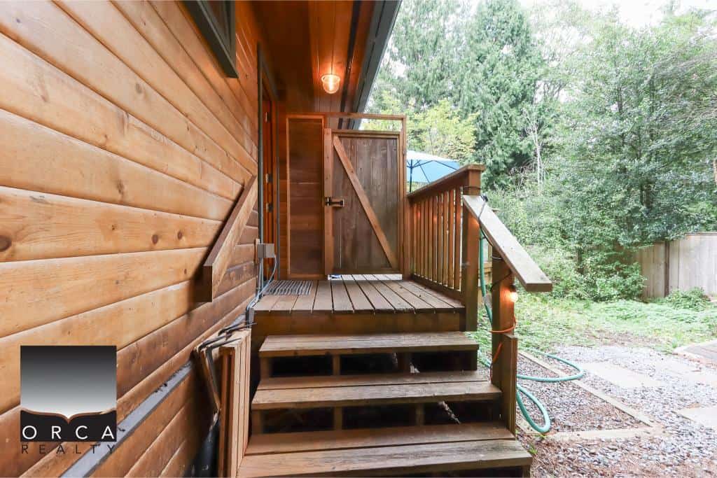 Charming wooden porch with steps and outdoor privacy, surrounded by lush greenery, ideal for relaxing and enjoying nature at Orca Realty Inc.