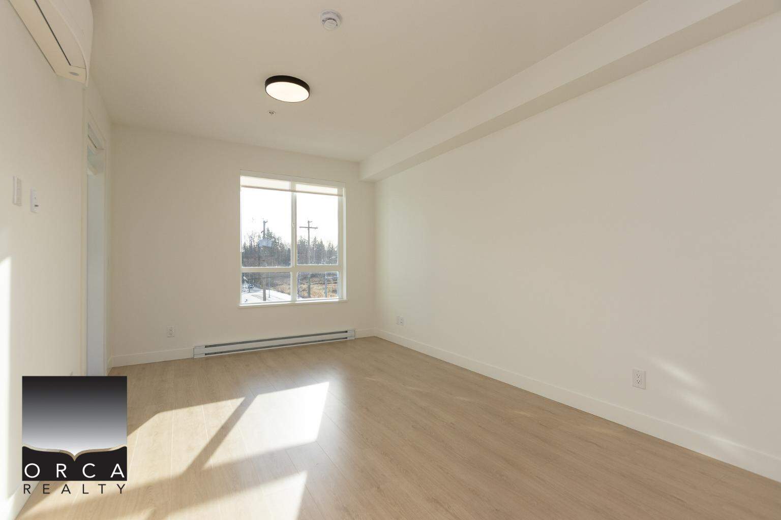 Bright empty living room in a modern condo built by Orca Realty Inc., featuring large window, light wood flooring, white walls, and natural sunlight, ideal for property buyers in Canada.
