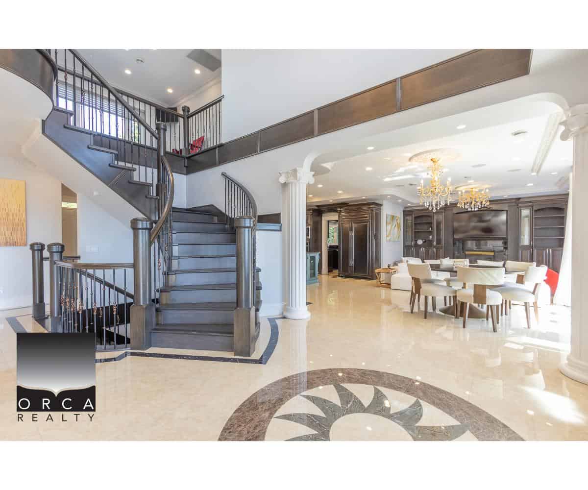 Elegant luxury home interior featuring a grand staircase with dark wood and metal balustrades, a spacious open living area with chandeliers, built-in cabinetry, and high-end finishes, ideal for upscale real estate listings.
