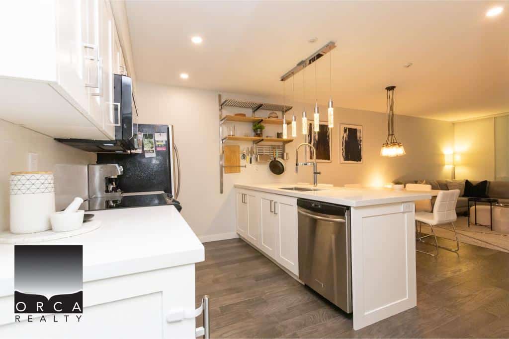 Modern open-concept kitchen with white cabinetry, stainless steel appliances, and stylish pendant lighting in a contemporary living space.
