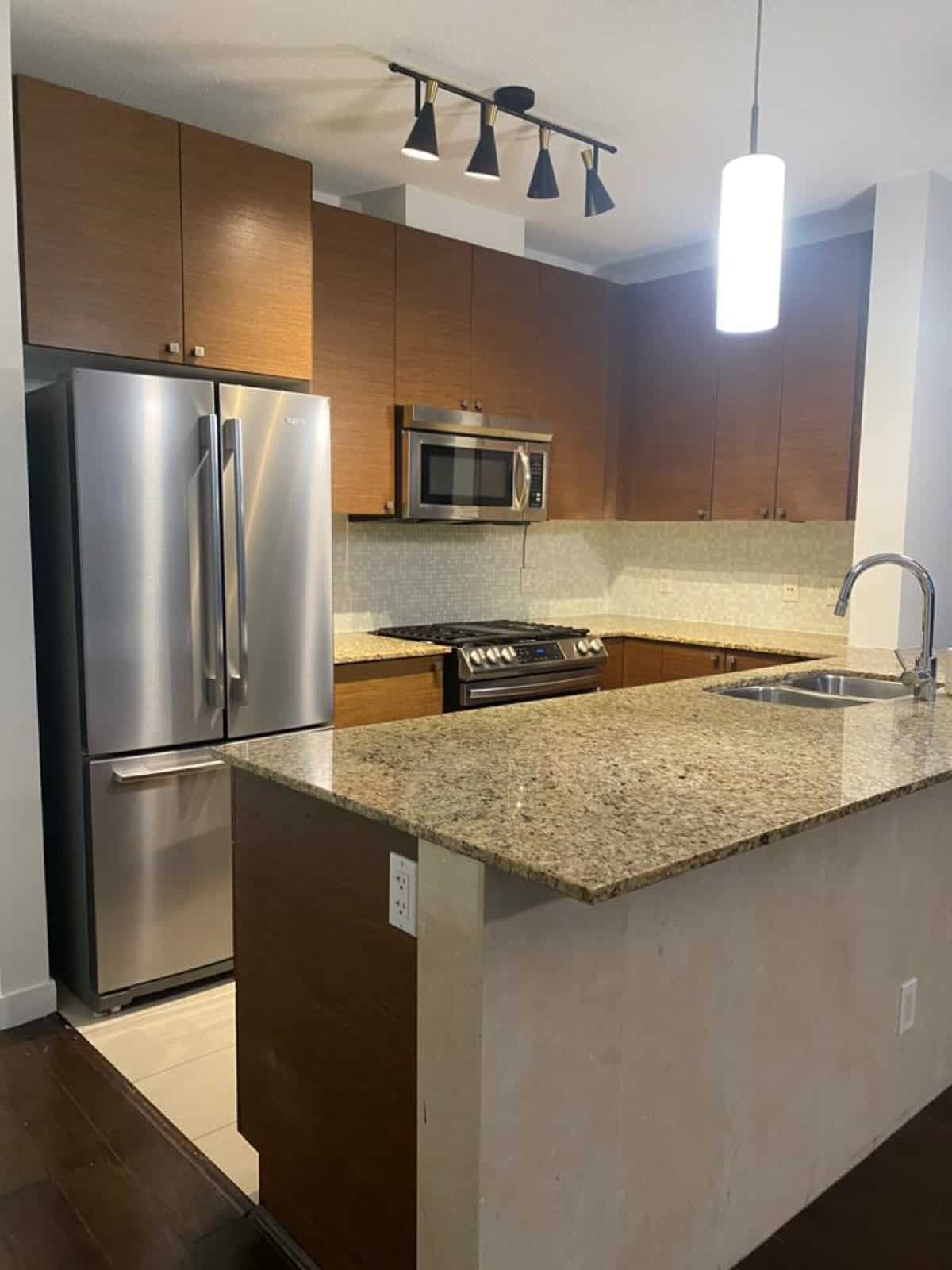 Modern kitchen with stainless steel fridge, microwave, gas stove, granite countertops, and wooden cabinetry, ideal for Vancouver real estate buyers.