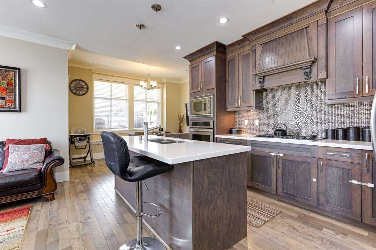 Spacious modern kitchen with dark wood cabinets, white countertop island, mosaic backsplash, stainless steel appliances, and hardwood floors, ideal for Vancouver real estate buyers.