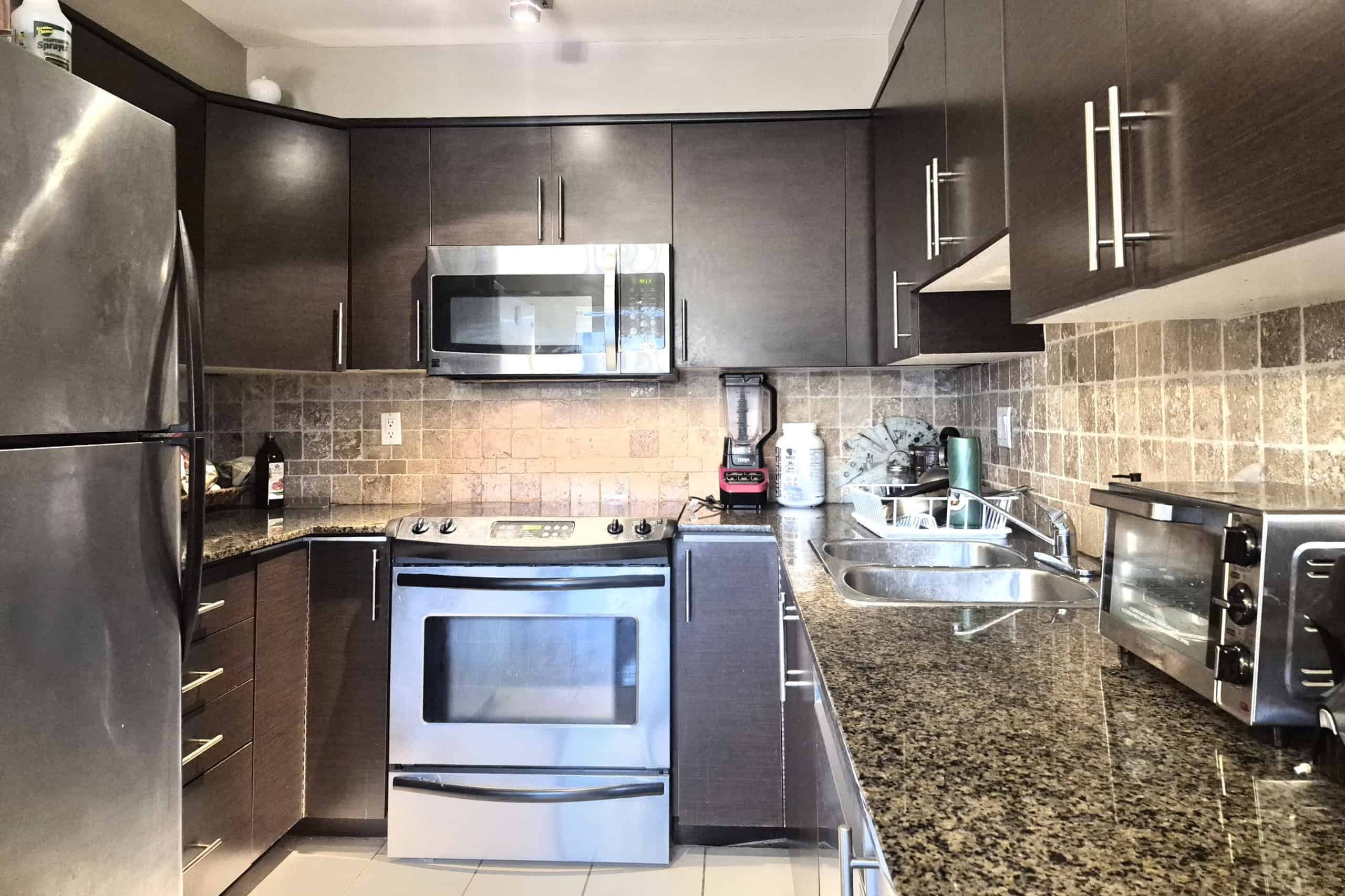 Bright modern kitchen with stainless steel appliances, dark wood cabinets, granite countertops, and a textured tile backsplash, showcasing upscale Vancouver real estate by Orca Realty Inc.