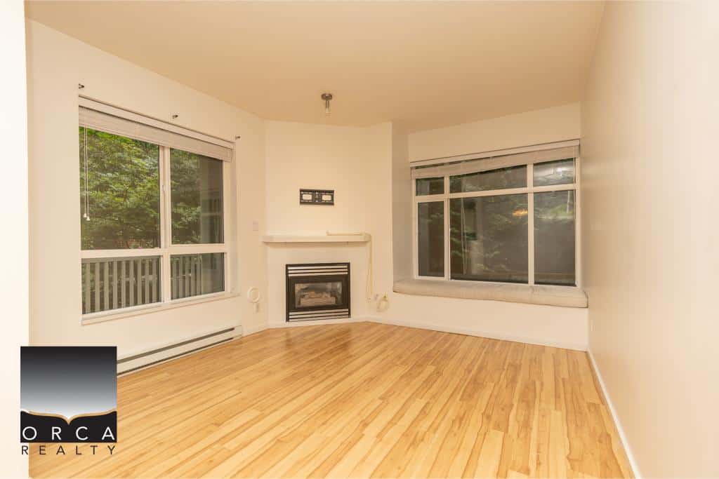 Bright living room with large windows and natural light, featuring hardwood floors, a cozy fireplace, and scenic views, perfect for Vancouver Island homebuyers seeking comfort and style.