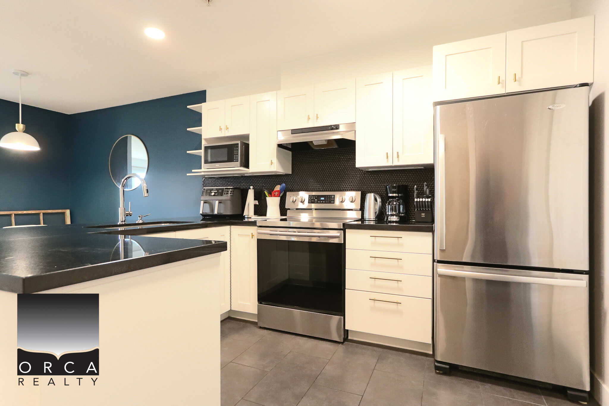 Bright modern kitchen with white cabinets, stainless steel appliances, black countertops, and a stylish blue accent wall, perfect for Vancouver real estate buyers.