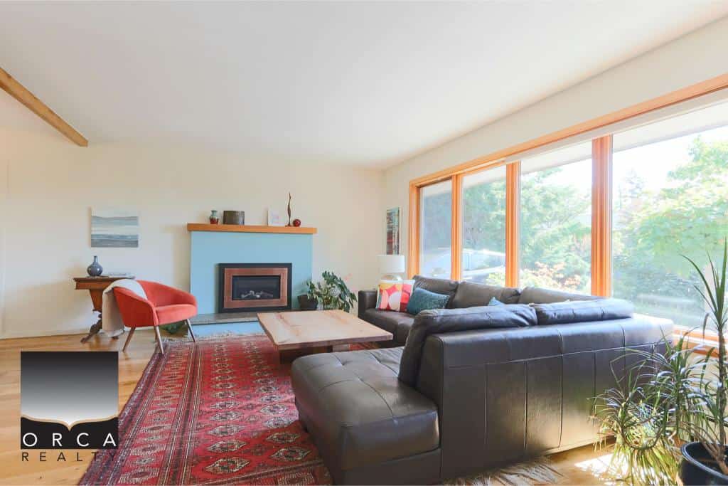 Bright living room with large windows showcasing green outdoor scenery, modern furniture, and cozy decor, ideal for Vancouver Island real estate and home buying in British Columbia.