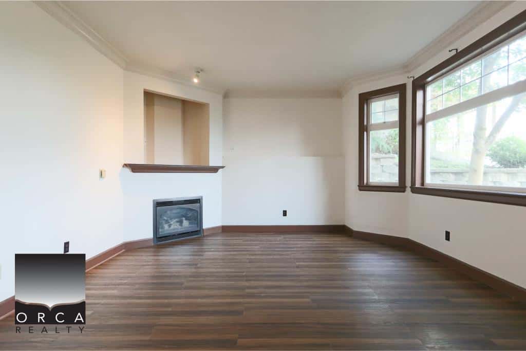 Bright spacious living room with large windows, hardwood floors, and a corner fireplace, ideal for homebuyers seeking a welcoming residence in Vancouver.