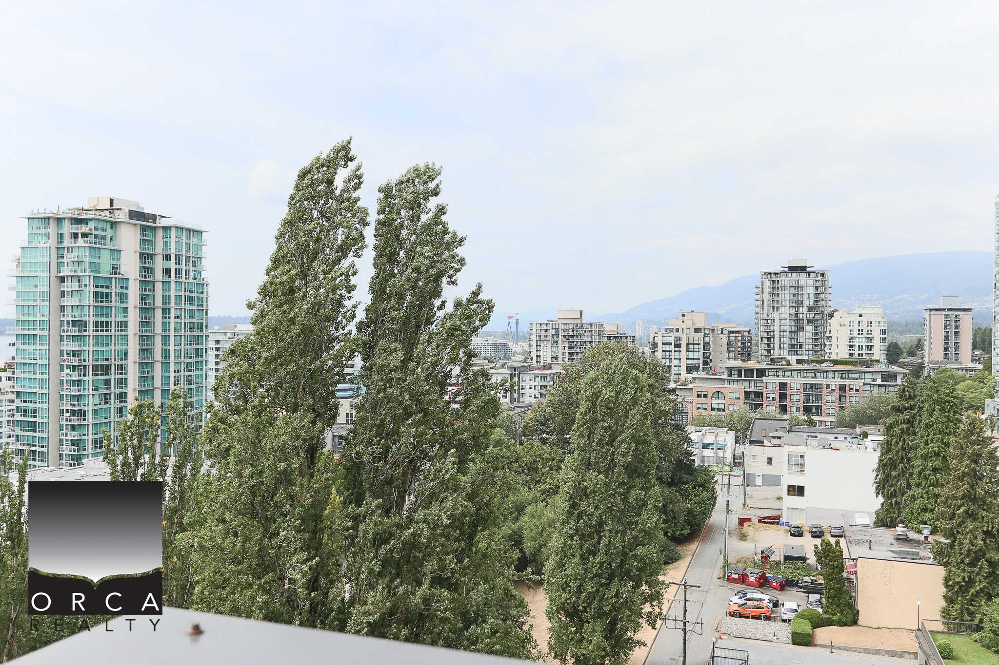 Modern urban skyline with high-rise condos and lush green trees in Vancouver, BC, viewed from a balcony during daytime, showcasing real estate excellence by Orca Realty Inc.