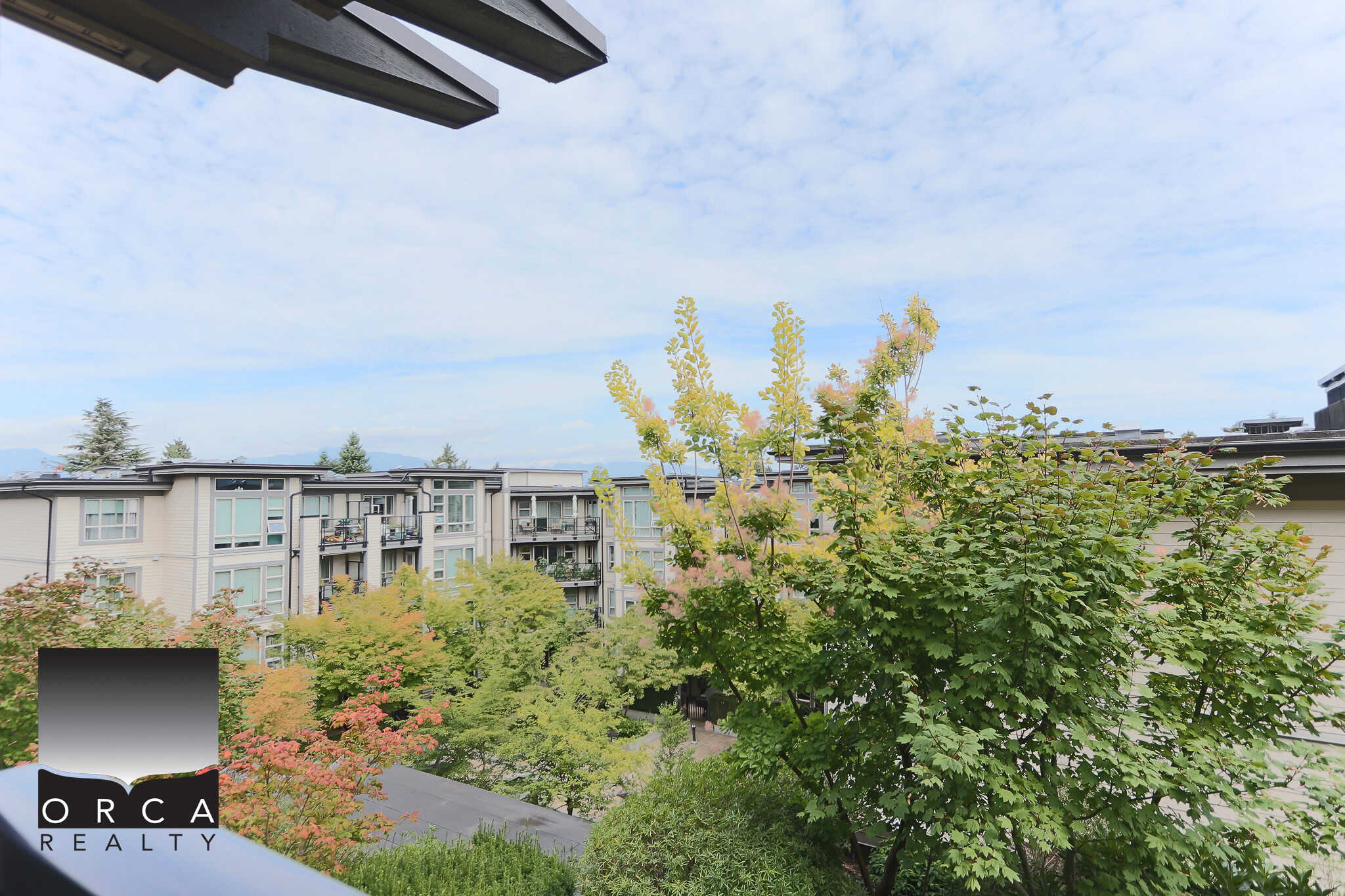 View of modern residential condos with lush green trees and a blue sky, showcasing Vancouver real estate properties managed by Orca Realty Inc.