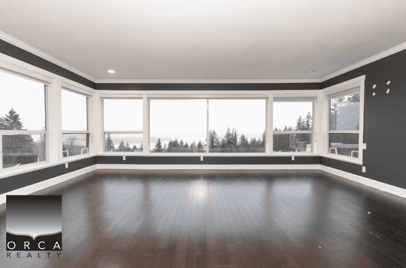 Bright spacious living room with large windows overlooking stunning ocean and forest views, ideal for coastal homes in Vancouver Island.
