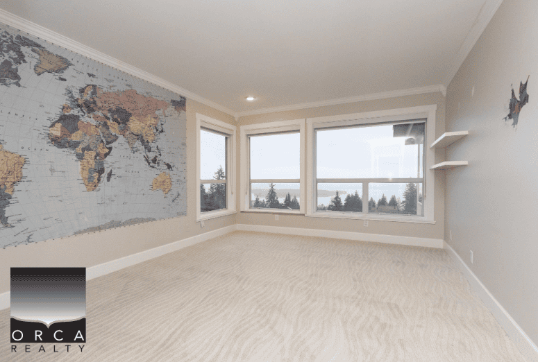 1. Bright, spacious room with large windows, world map wall decor, and ocean views, ideal for Vancouver Island real estate opportunities.