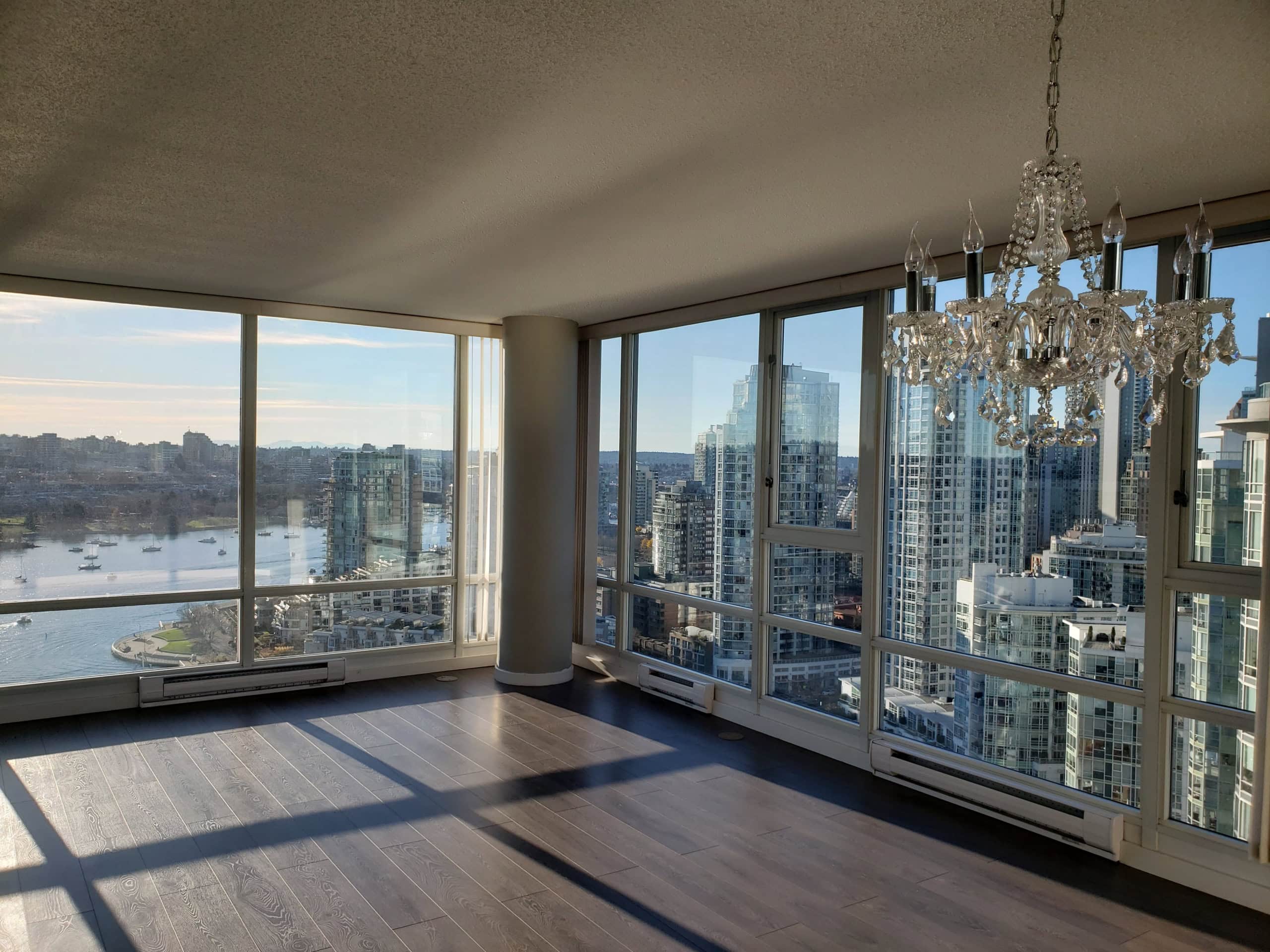 Stunning high-rise apartment with panoramic city and water views, featuring floor-to-ceiling windows, hardwood floors, and a luxurious chandelier, ideal for modern Vancouver living.