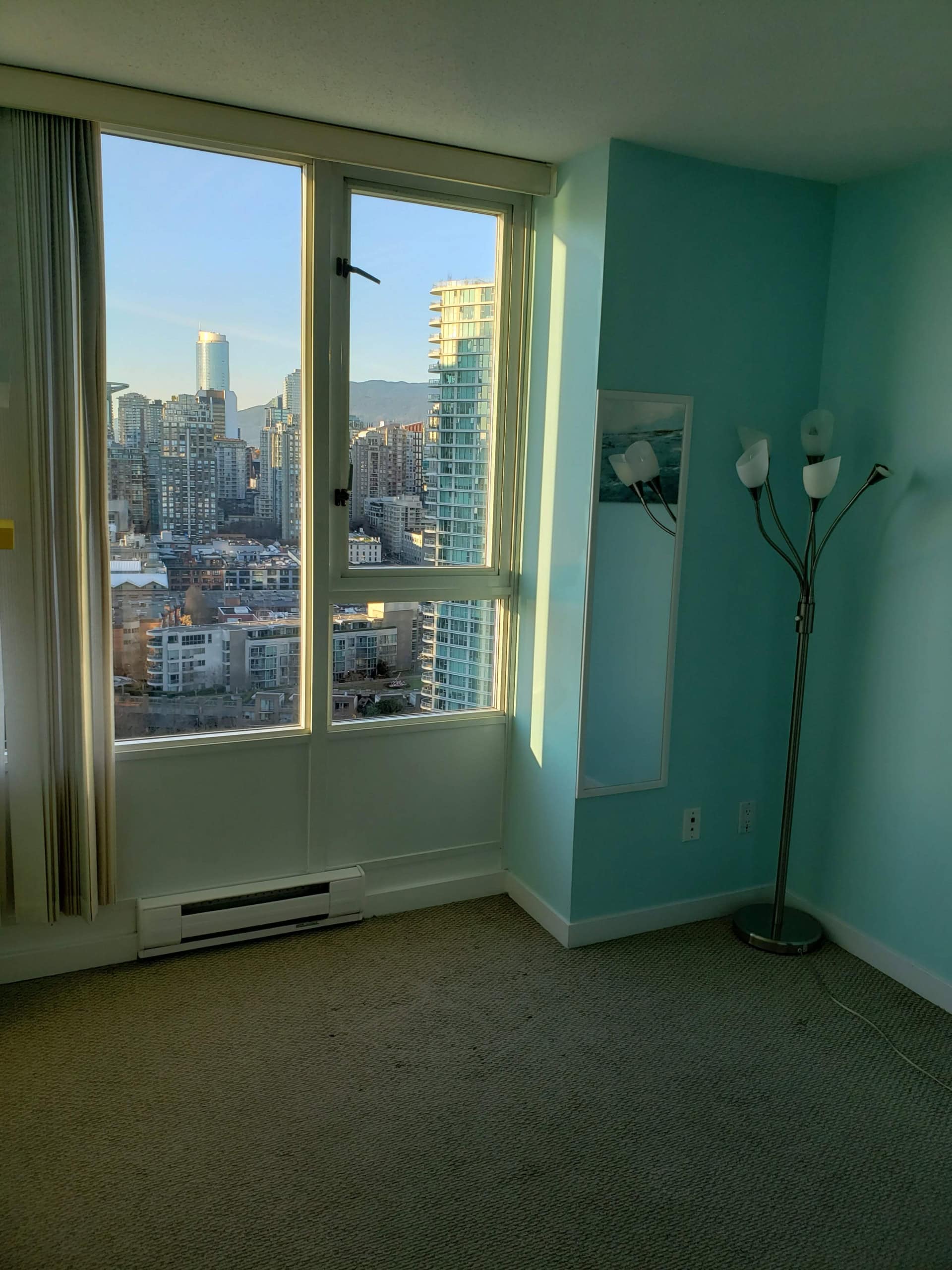 Panoramic city view from high-rise condominium window in Vancouver, BC, showcasing modern urban skyline and mountain backdrop, ideal for downtown Vancouver real estate listings.