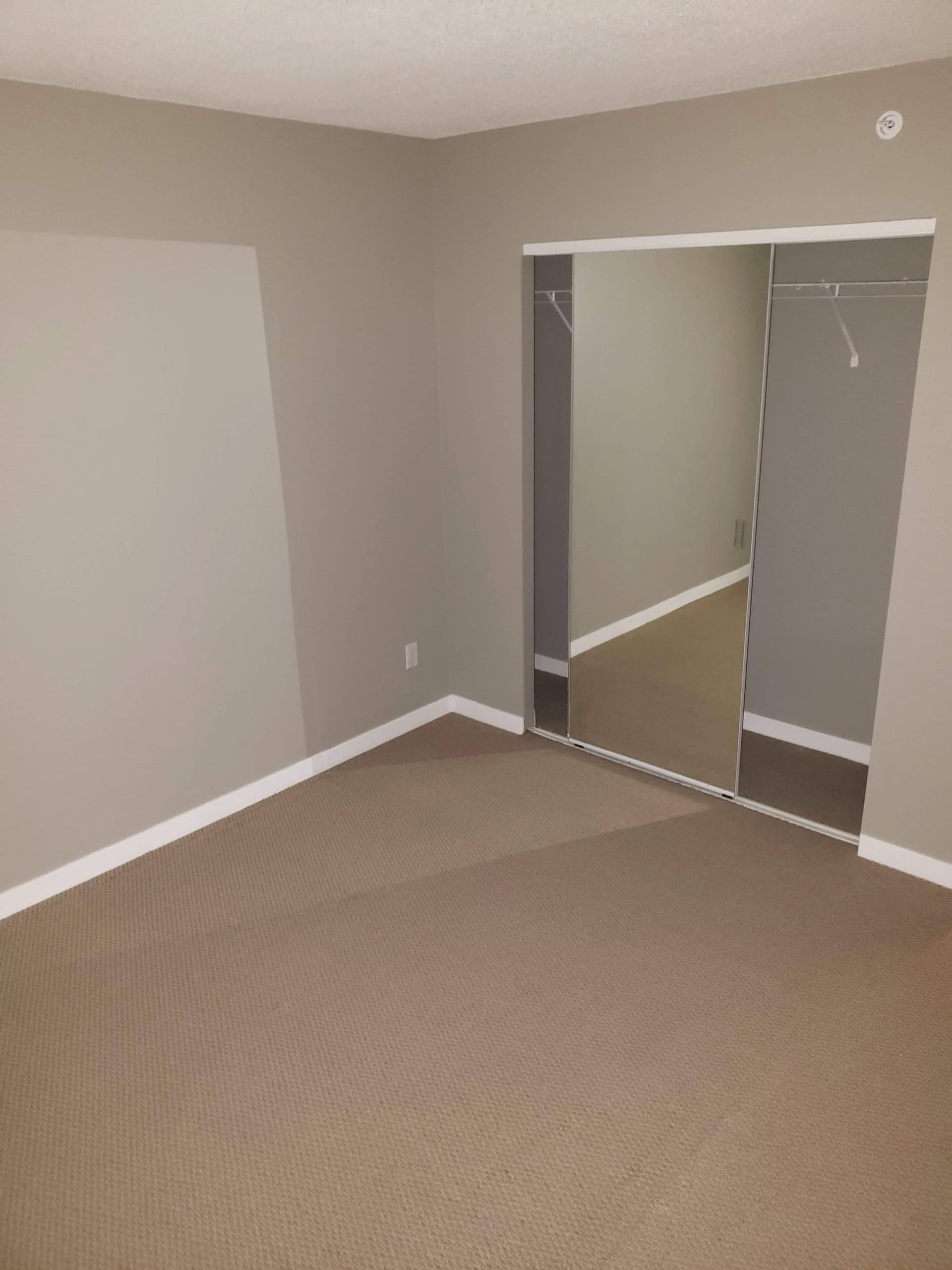 Spacious bedroom with beige carpet and mirrored closet doors, ideal for comfortable living and storage solutions in a modern property listed by Orca Realty Inc.