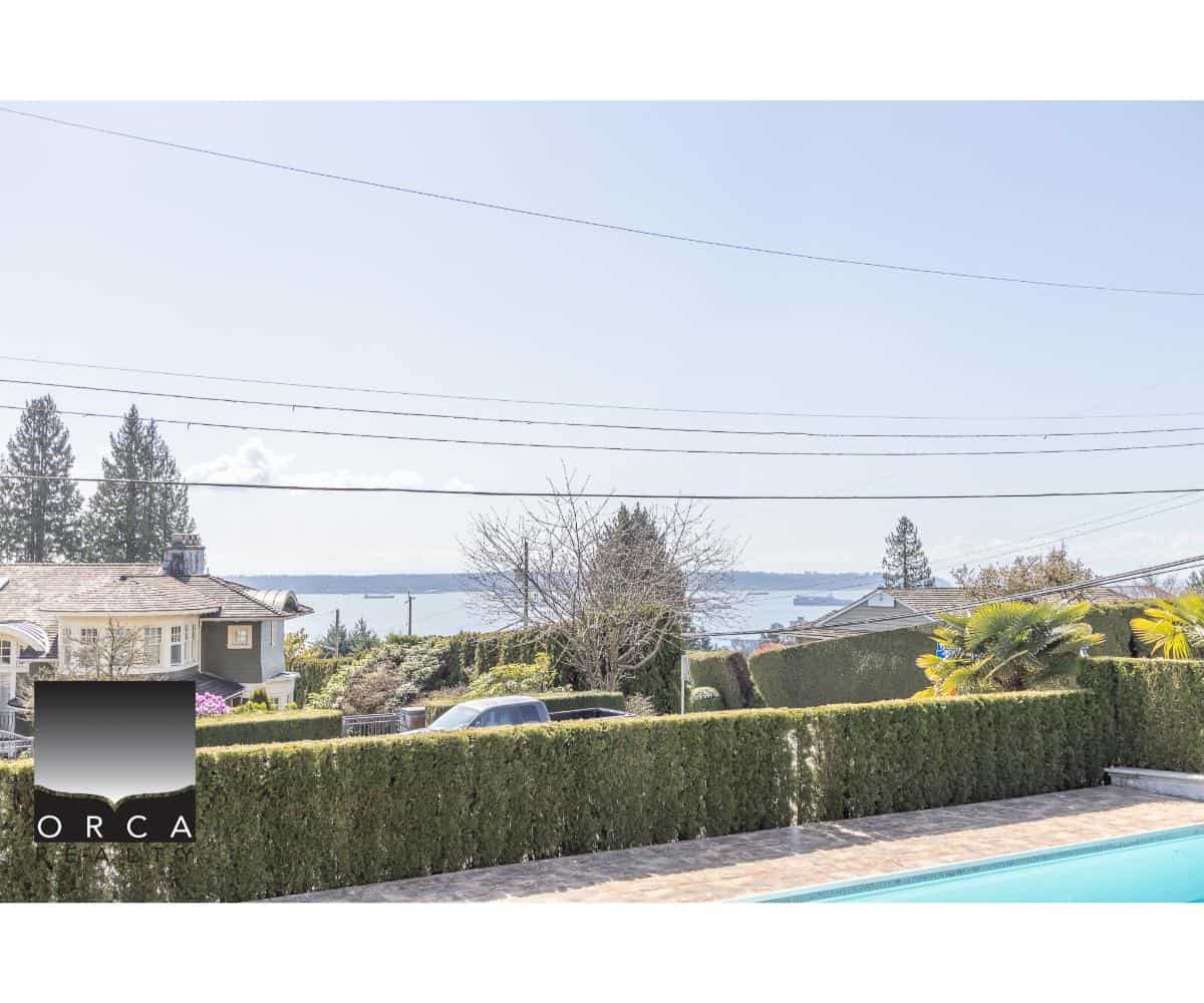 View of ocean and neighborhood from property with lush greenery and hedges in Orca Realty Inc. listing, showcasing prime waterfront real estate in a scenic, tranquil setting in Vancouver Island, BC.