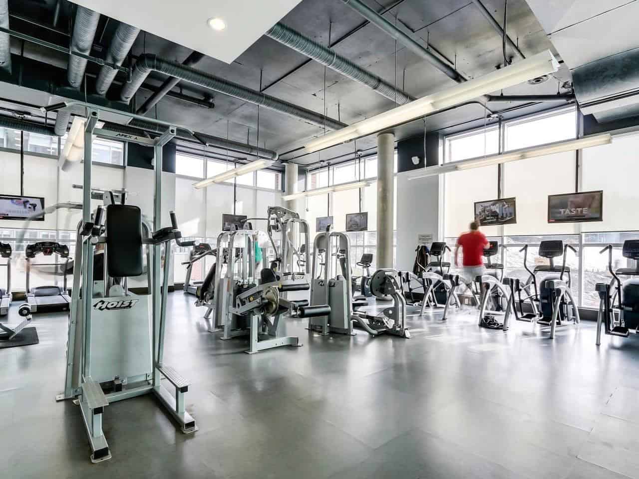 Modern fitness centre with gym equipment and workout machines, bright natural light, sleek industrial design, ideal for health-conscious tenants, available in commercial and residential properties.