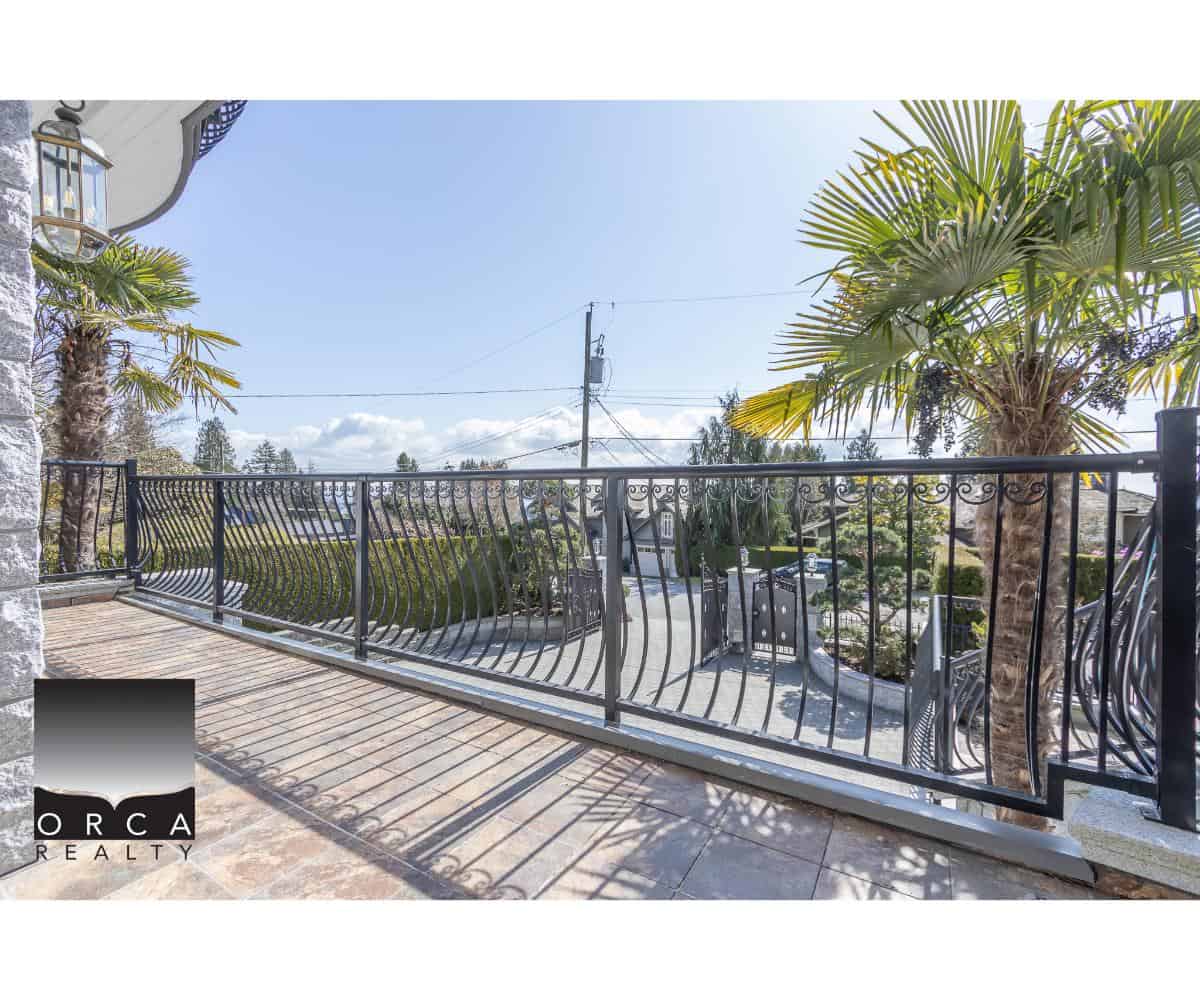 Balcony view with wrought iron railing, tropical palm trees, and outdoor seating at Orca Realty Inc. showcasing quality real estate in Victoria, BC.