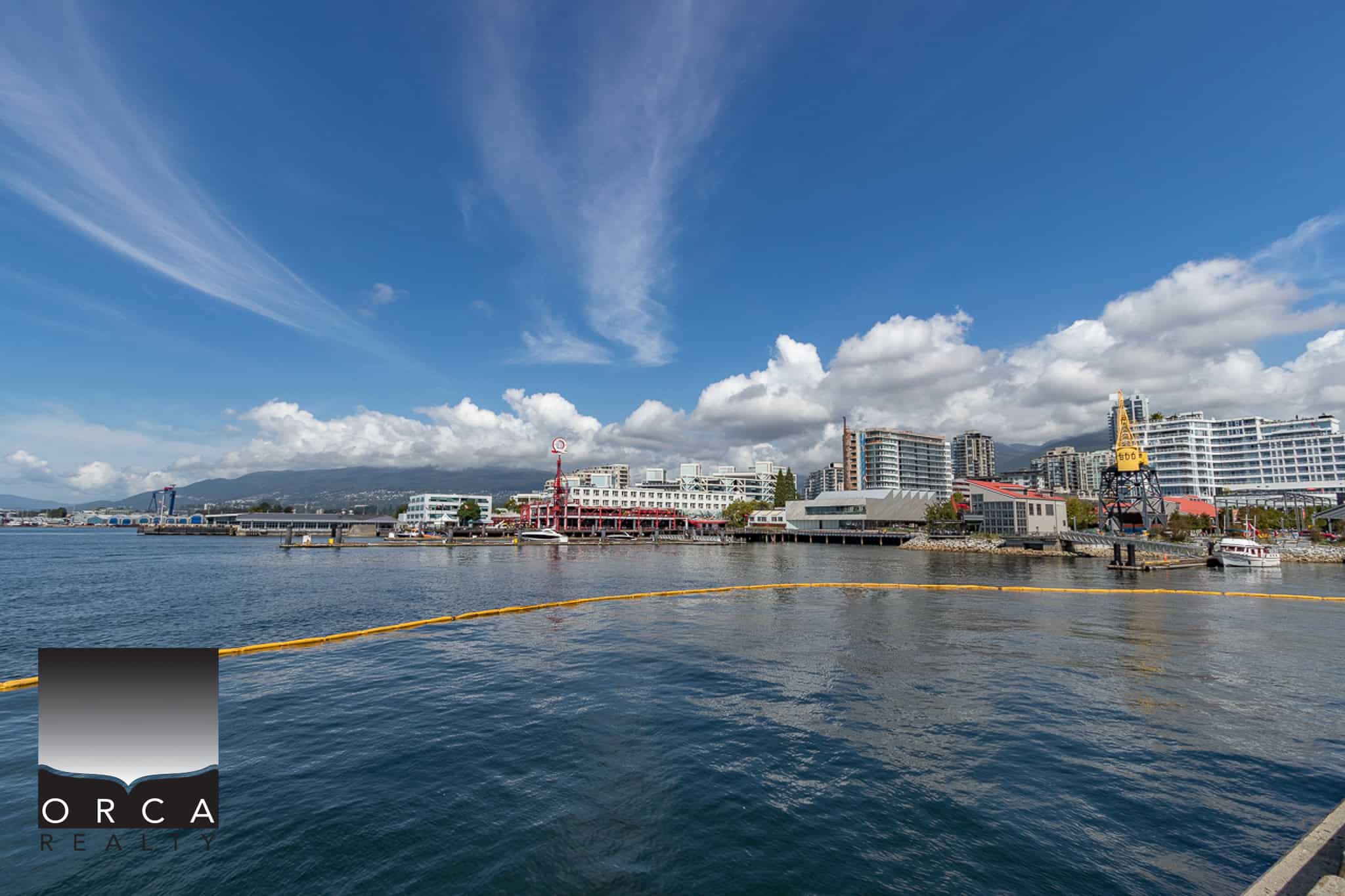 Vancouver waterfront cityscape with modern buildings, harbor, and blue sky, representing prime real estate opportunities by Orca Realty Inc.