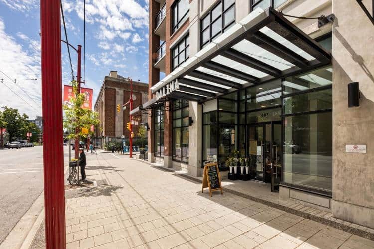 Modern commercial building entrance with glass storefronts and outdoor seating, located in a vibrant urban downtown area. Perfect for retail or office tenants seeking prime real estate.