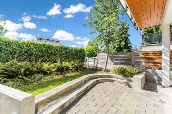 Contemporary outdoor patio in Vancouver featuring lush greenery, a curved concrete bench, and a paved area, ideal for relaxing or entertaining at 101-7878 Granville Street.