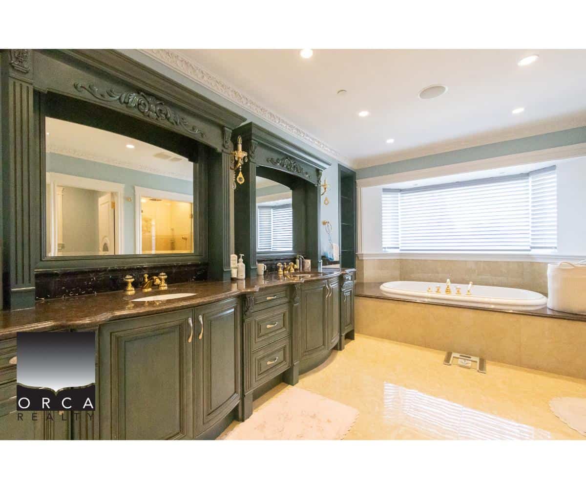 Luxurious bathroom with dark wooden vanity, gold fixtures, large mirror, and a relaxing bathtub near a bay window with horizontal blinds. Elegant design perfect for Vancouver real estate.