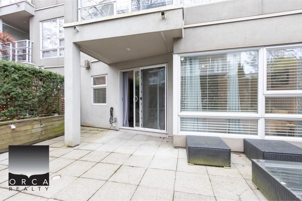 Spacious outdoor patio area of a modern city condo with sliding glass door, outdoor furniture, and large windows, ideal for real estate listings in Vancouver.