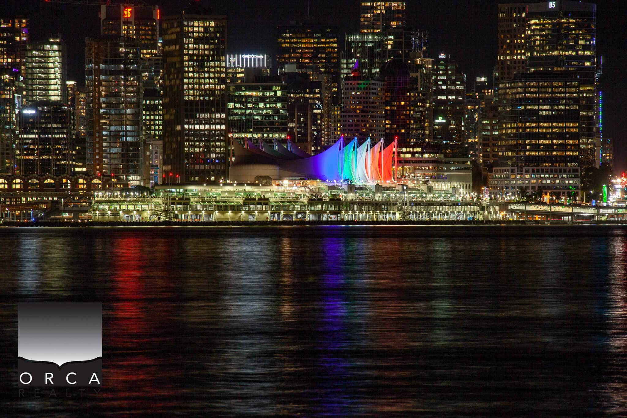 Vibrant night skyline of Vancouver with colourful lights illuminating Canada Place and surrounding skyscrapers, showcasing prime real estate opportunities with Orca Realty Inc.
