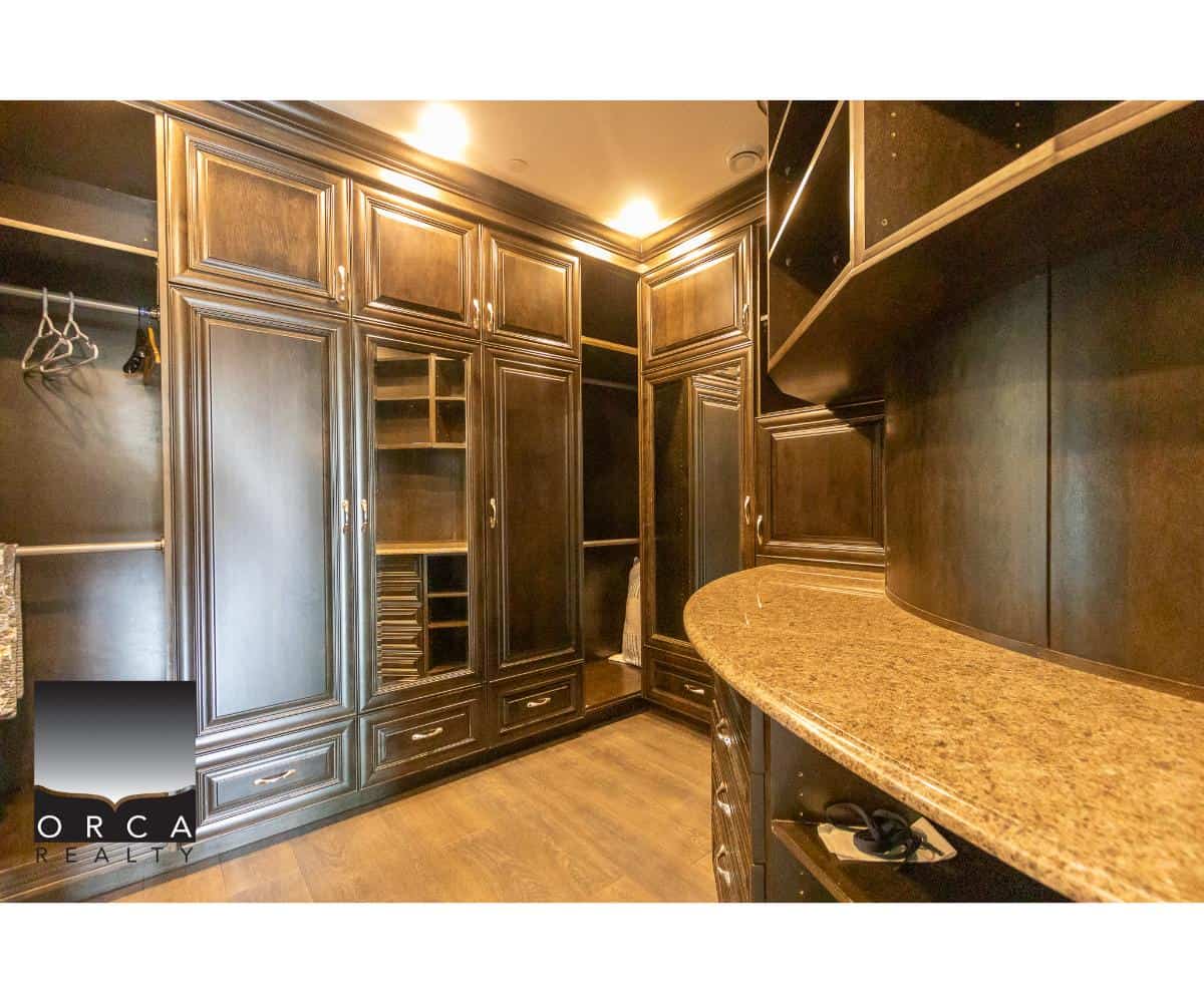 Closet with dark wood cabinetry and granite countertop, featuring ample storage, shelves, and hanging space. Perfect for luxury real estate and upscale home organization in Ontario.
