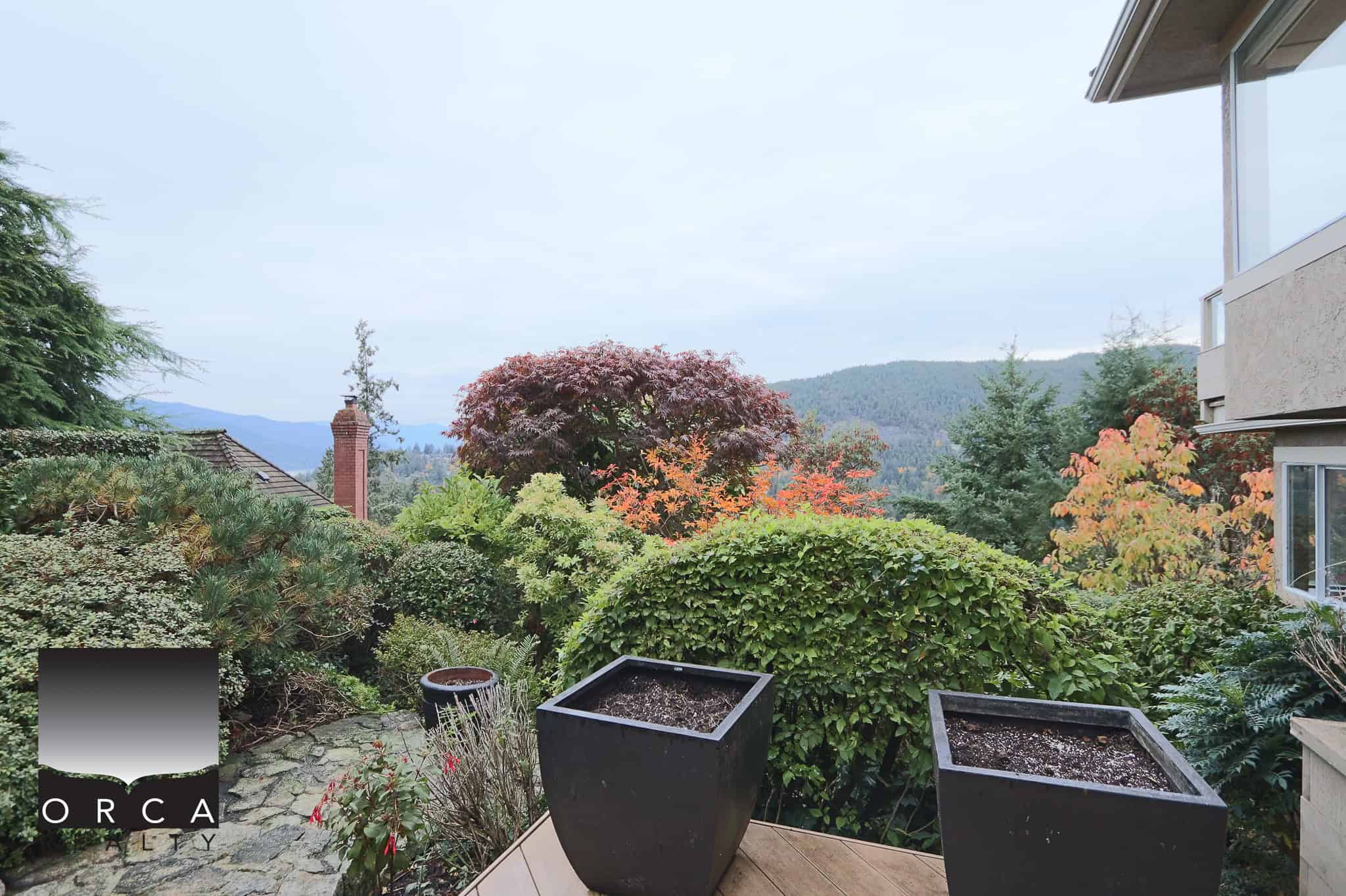 Vibrant garden view with lush greenery, colorful trees, and mountain scenery, perfect for Vancouver Island real estate and outdoor living enthusiasts.