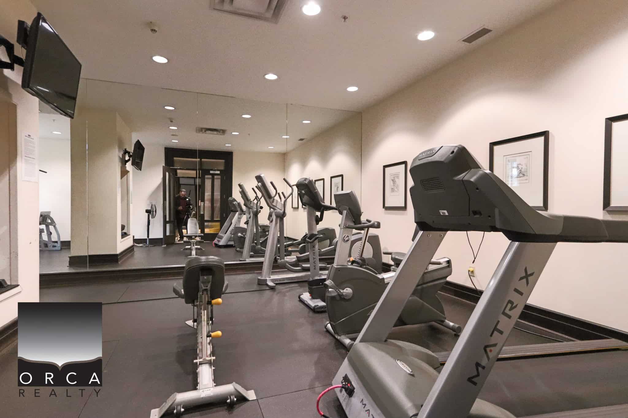 Fitness center with cardio equipment at 203-170 W 1st Street, North Vancouver, featuring treadmills, stationary bikes, and weights, ideal for health-conscious residents.