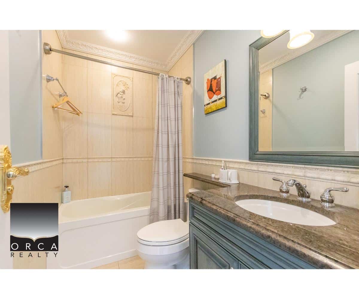 Elegant bathroom with bathtub, shower, and vanity featuring a granite countertop, ample mirror, and classic décor, showcasing luxury home features from Orca Realty Inc.
