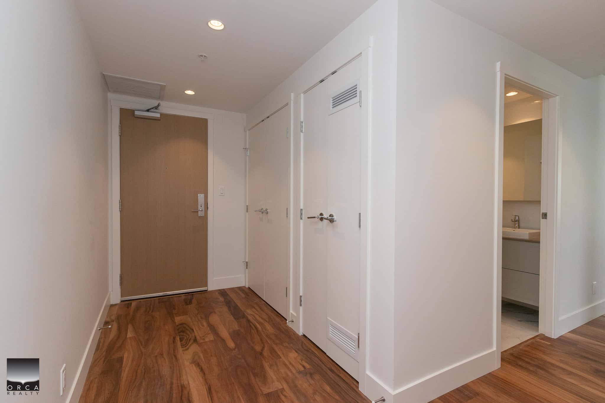 Spacious apartment entryway with hardwood floors, modern closet doors, and a neutral colour palette, showcasing the stylish interior design of Orca Realty Inc. property in Vancouver.