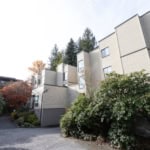 Contemporary multi-story residential buildings with beige siding surrounded by lush greenery and trees displaying fall foliage, showcasing modern architecture ideal for Vancouver real estate.